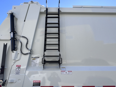 Truck side with vertical ladder on the dump body, hydraulic cylinder, and safety stickers visible.