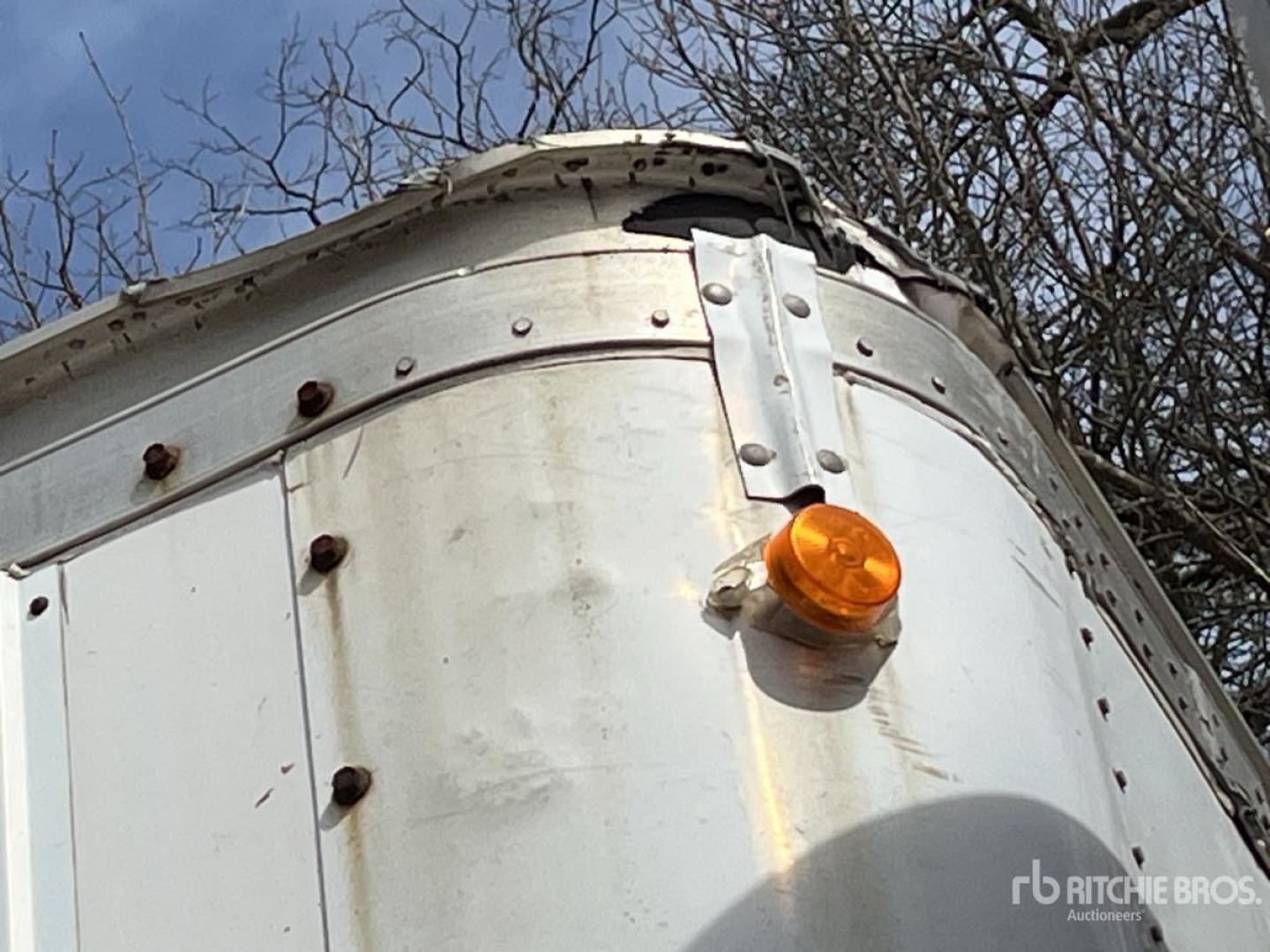 Trailer front corner with rounded aluminum skin, orange clearance light, riveted seams, and trees in background.