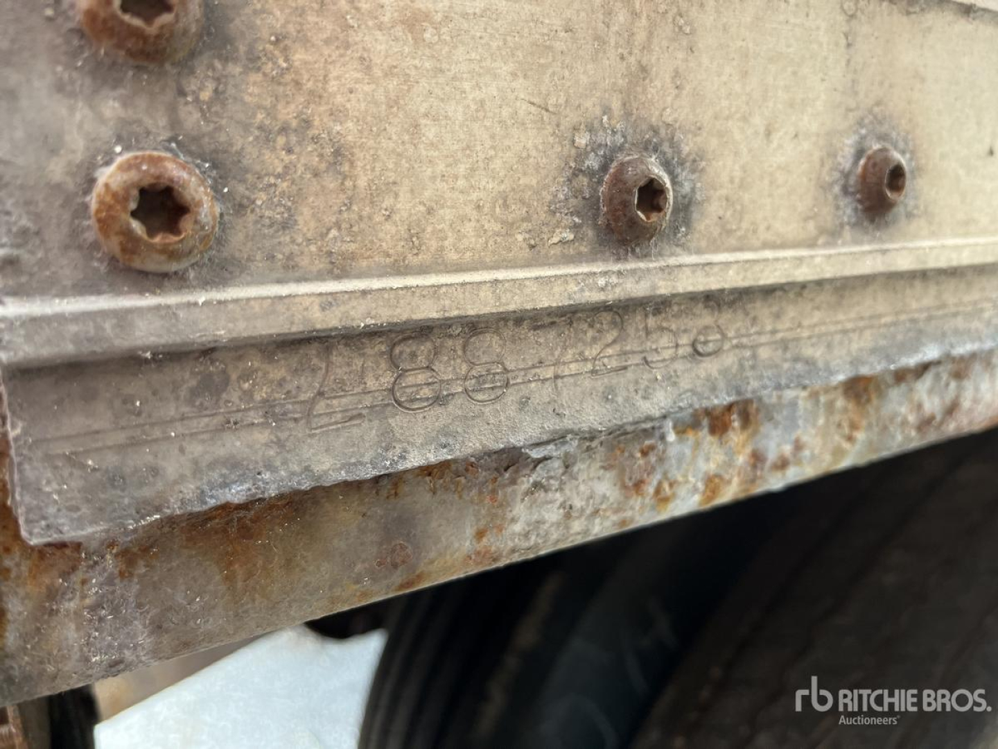 Vehicle trailer side with rusted lower edge and embossed lettering; visible bolts and a portion of a wheel well.