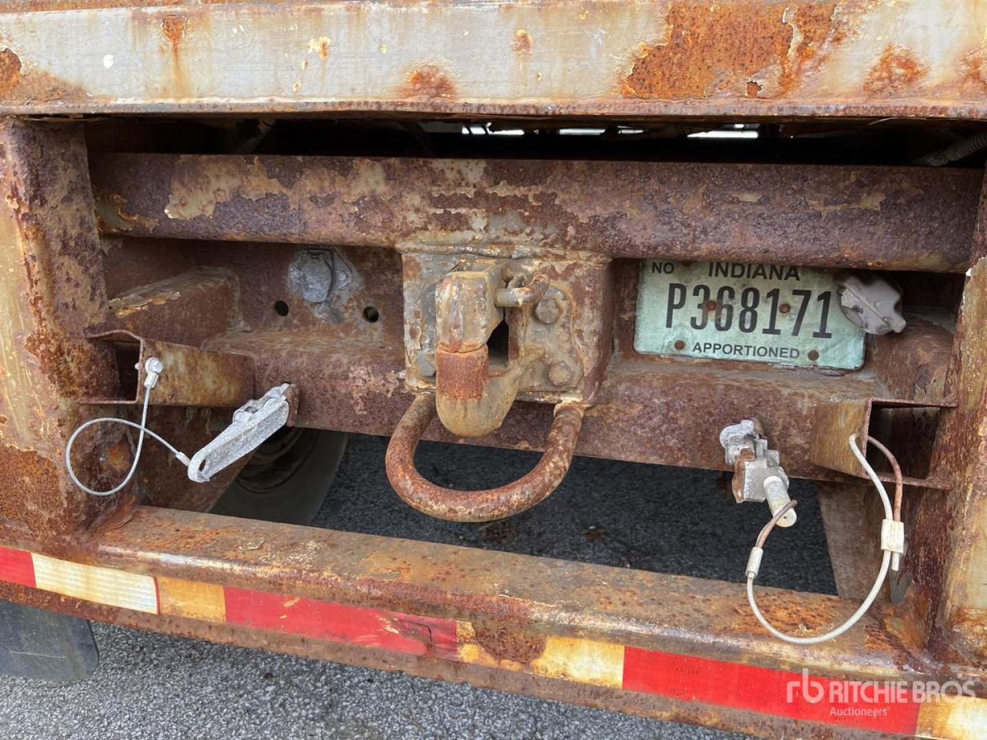 Rear of a rusty trailer hitch area showing a rusted hitch ring, electrical connectors, and a license plate. Visible text includes 'INDIANA P368171', tag details, and various wires.