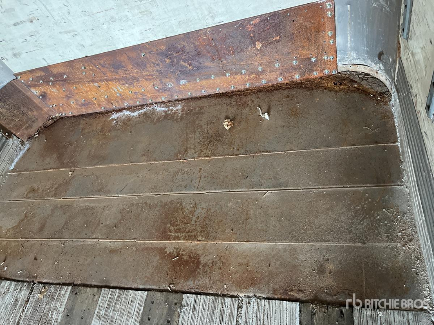 Trailer interior floor with brown metal planks and riveted joints, showing signs of use and soil buildup.