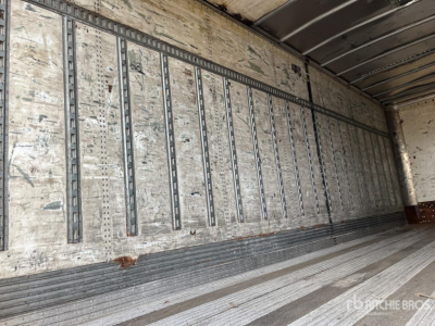 Interior trailer wall with vertical slats and metal tracks, weathered plywood panels, and a ribbed floor.