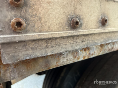 Vehicle trailer side with rusted lower edge and embossed lettering; visible bolts and a portion of a wheel well.
