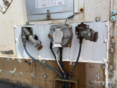 Trailer rear utility panel with hoses and valves, central gray valve assembly, left pressure fitting with blue hose, right rusty valve, sheet metal panel, bolts, and wiring harnesses.