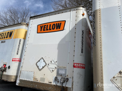 Trailer rear with Yellow logo and warning labels, white body, deck trailer, stacked with other trailers.