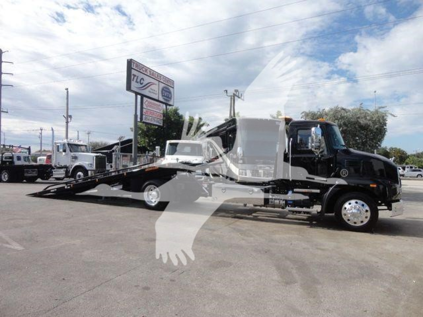Truck: 2026 Mack MD6 rollback w/ flatbed in carrier lot; black cab, white flatbed area, loading ramp visible.