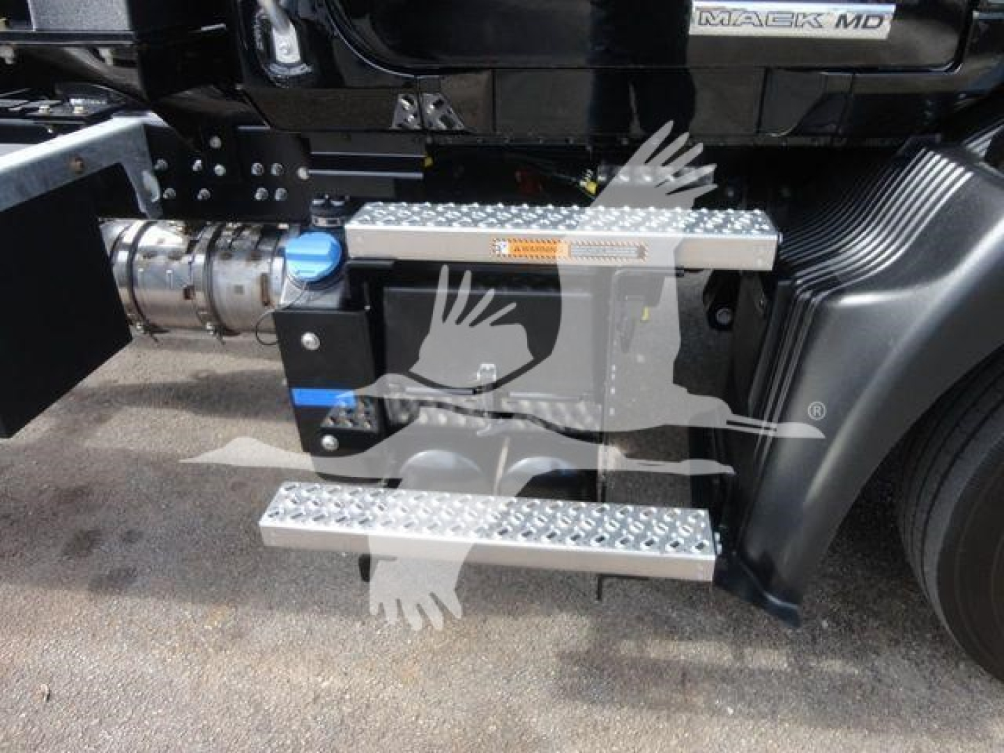 Mack MD6 truck side with aluminum diamond-plate steps and blue fill cap, showing chassis area and drivetrain components.