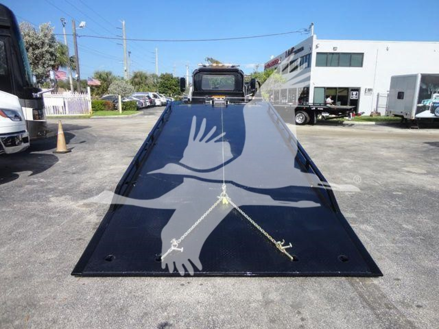 Mack MD6 rollback bed with hydraulic ramps, black paint, safety decals, and tiedown straps in a dealership lot.