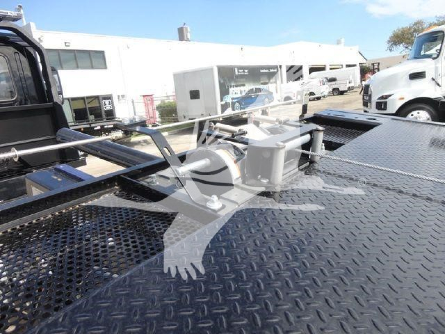 View of a Mack MD6 rollback truck work area on a diamond plate metal deck with hydraulic components and winch in foreground.