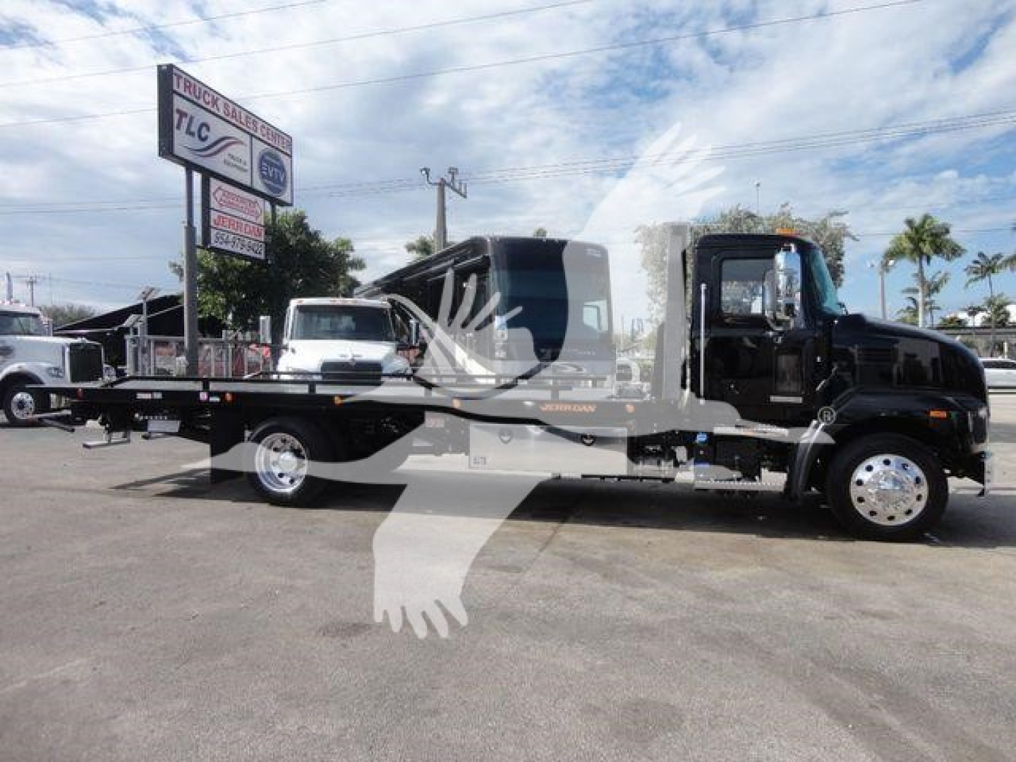 Mack MD6 rollback tow truck in service bay showing Mack branding and wheel-lift bed.