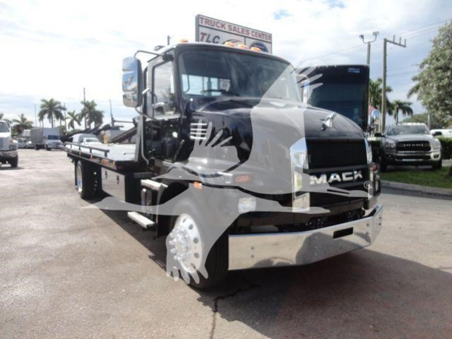 Mack MD6 rollback truck shown in dealership lot with chrome bumper and black cab, front grille with Mack badge, flatbed extended.
