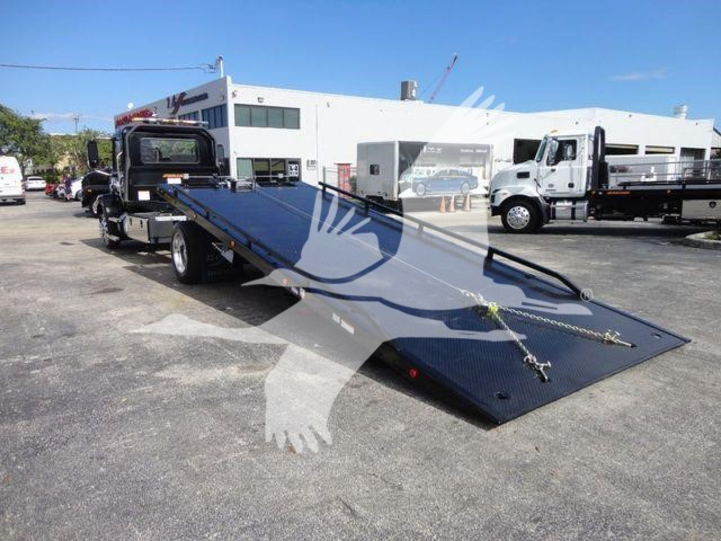 Truck bed with a ramp extended, Mack MD6 rollback truck in a dealership lot.