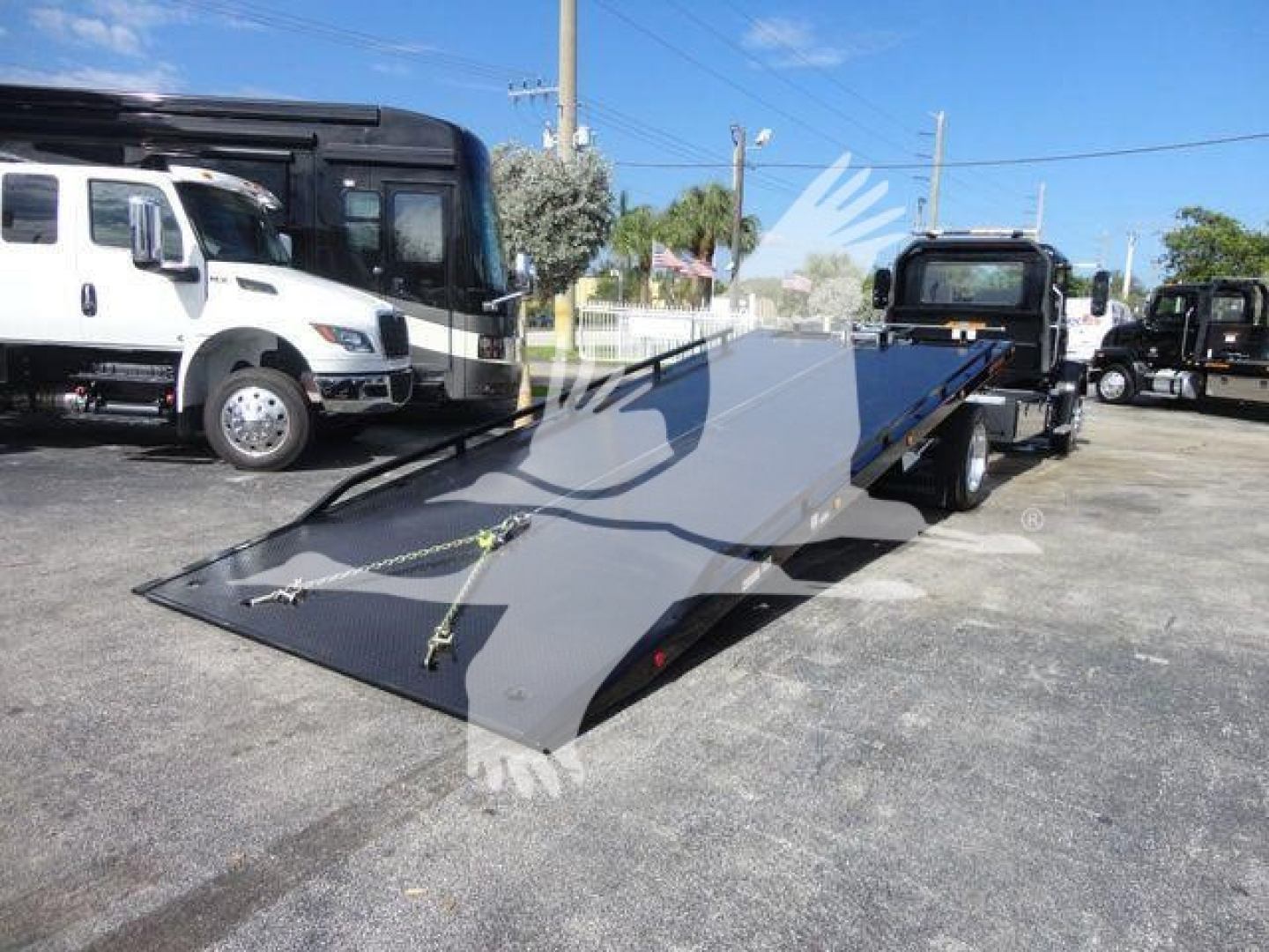 MD6 roll-back tow truck with loading ramp extended showing new in-stock condition, on a dealership lot among other trucks.