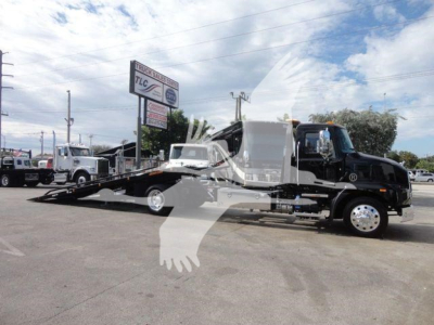 Truck: 2026 Mack MD6 rollback w/ flatbed in carrier lot; black cab, white flatbed area, loading ramp visible.