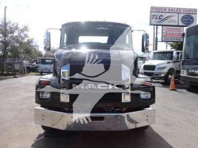 Front view of a black Mack MD6 truck with large chrome bumper; dealership lot in background with signs and other trucks.