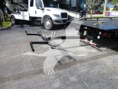 Trucker’s platform with a Mack MD6 rollback truck in background; front hitch and tow arms extended in foreground; white vehicle and parking lot.