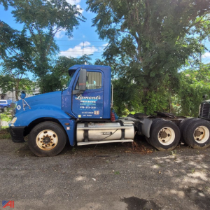 Blue Freightliner Columbia 120 conventional truck cab side view showing large fuel tanks and dual rear axles, with letters Lement's Rigging on door and contact phone on cab.