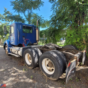 Blue Freightliner Columbia 120 truck chassis with no cab, exposed dual rear axles and tires, side exhaust, rear mudflaps, in a gravel lot.