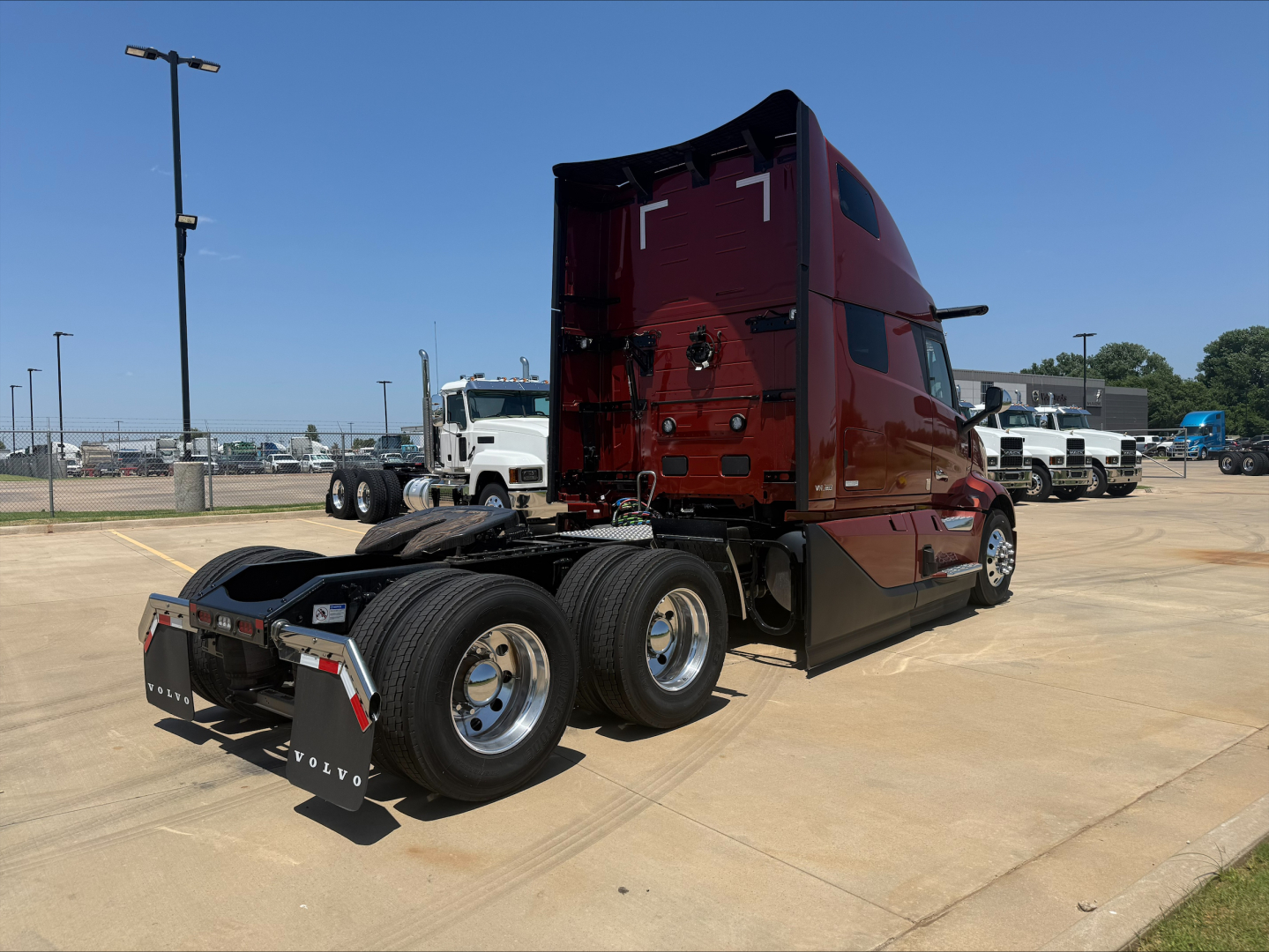 Volvo VNL64T860 cab with maroon exterior showing rear view and dual rear axles in a dealership lot.
