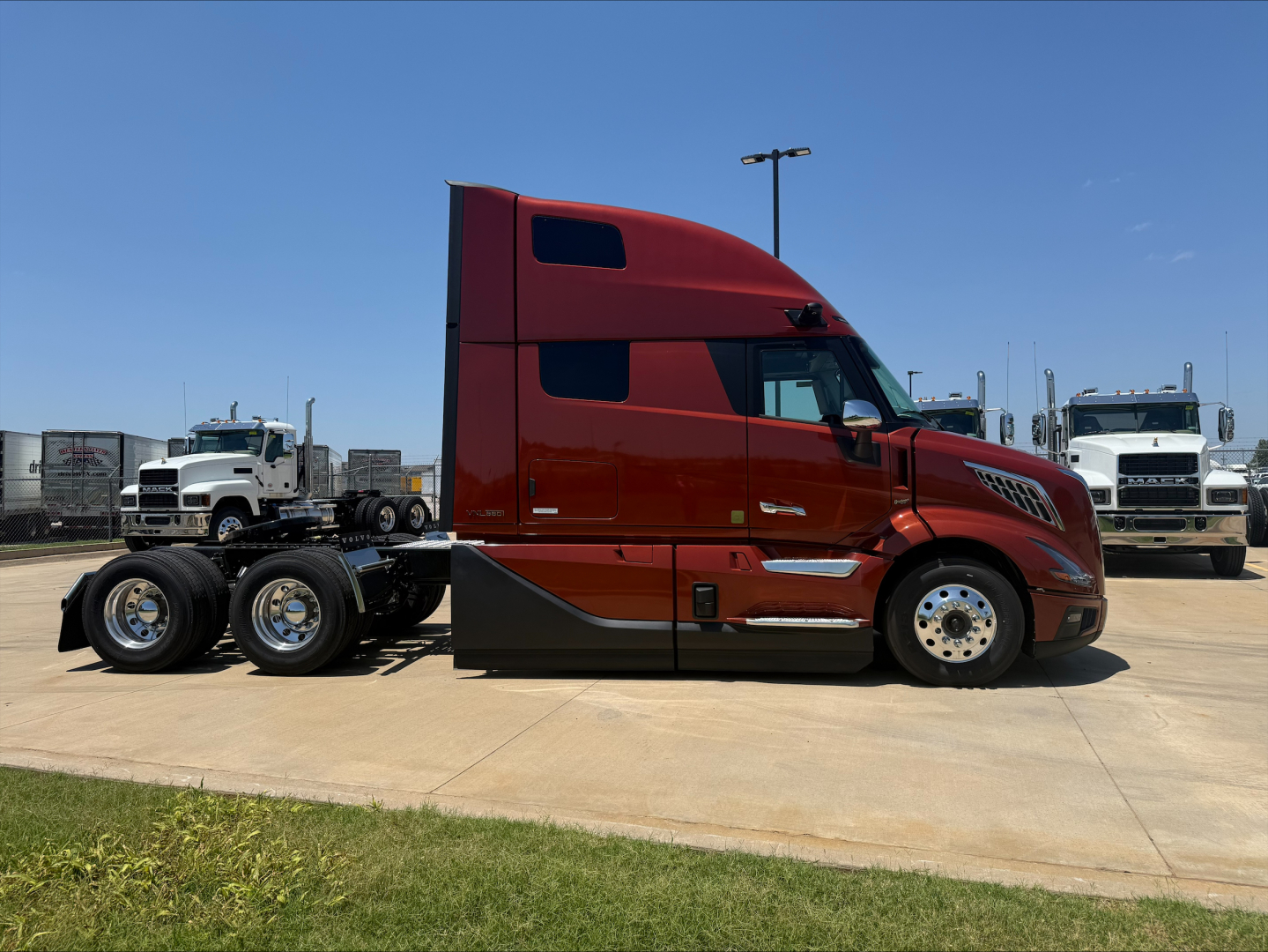 Red Volvo VNL64T860 semi-truck cab in a dealership lot, side view with dual rear axles, chrome wheels, and fuel tanks visible.