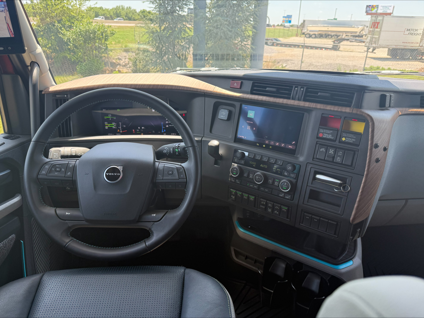 Volvo truck cockpit showing steering wheel, digital gauge cluster, and center touchscreen display with control buttons.