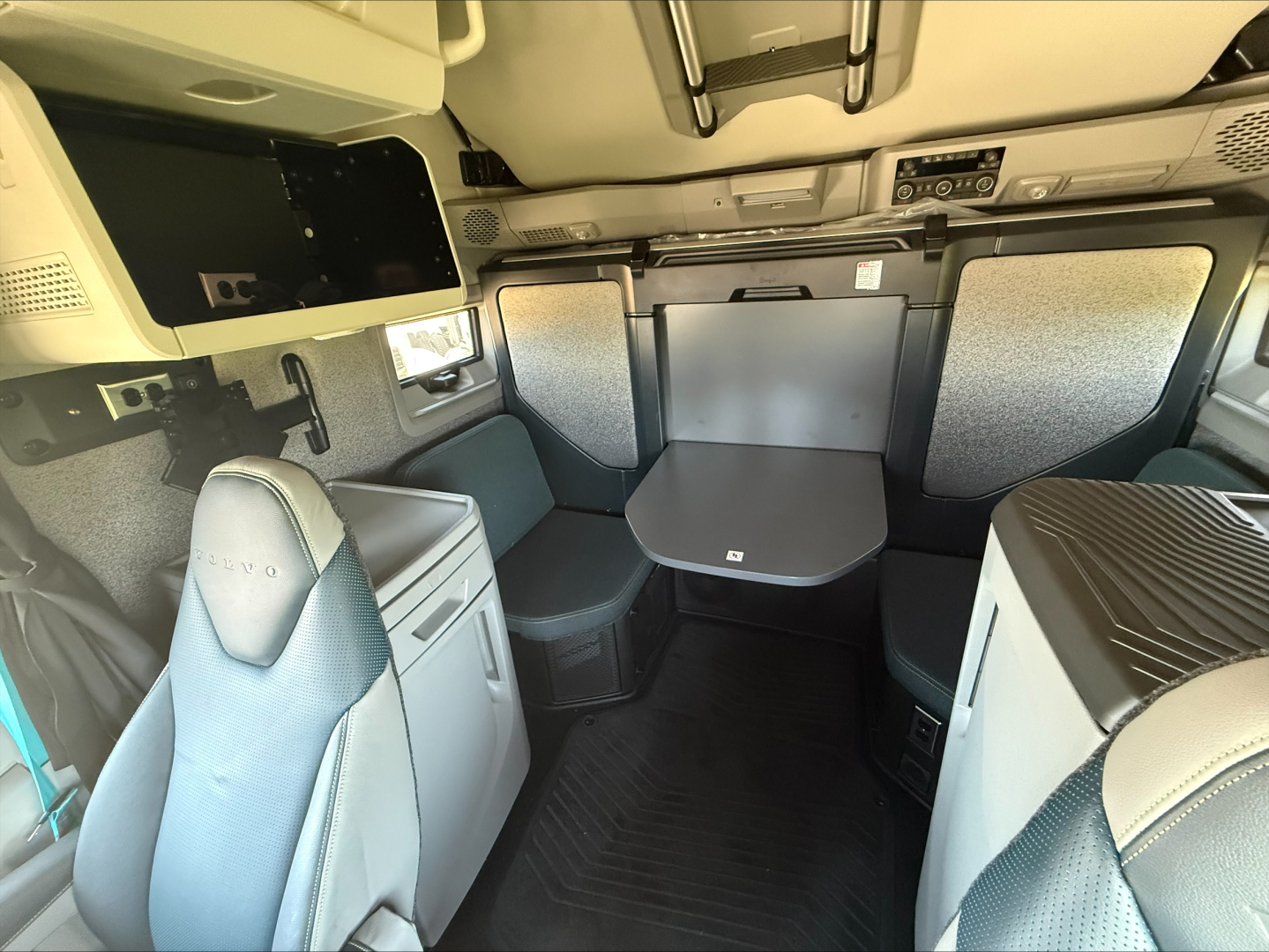 Cab interior of a 2026 Volvo VNL64T860 in-conventional sleeper showing captain seat, side cabinets, table, and seating area.