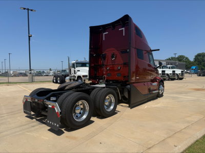 Volvo VNL64T860 cab with maroon exterior showing rear view and dual rear axles in a dealership lot.