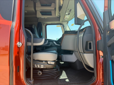 Interior of a 2026 Volvo VNL64T860 cab with front seats and dashboard visible through open door. Includes steering column, driver seat controls, and floor mat.