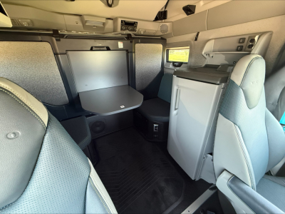 Truck cab interior of a 2026 Volvo VNL64T860 showing seating, table, and compact kitchenette with fridge.