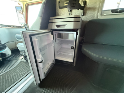 Volvo VNL64T860 interior showing compact mini fridge/freezer unit with open doors, located in cab beside seating area, compact appliance with storage shelves.