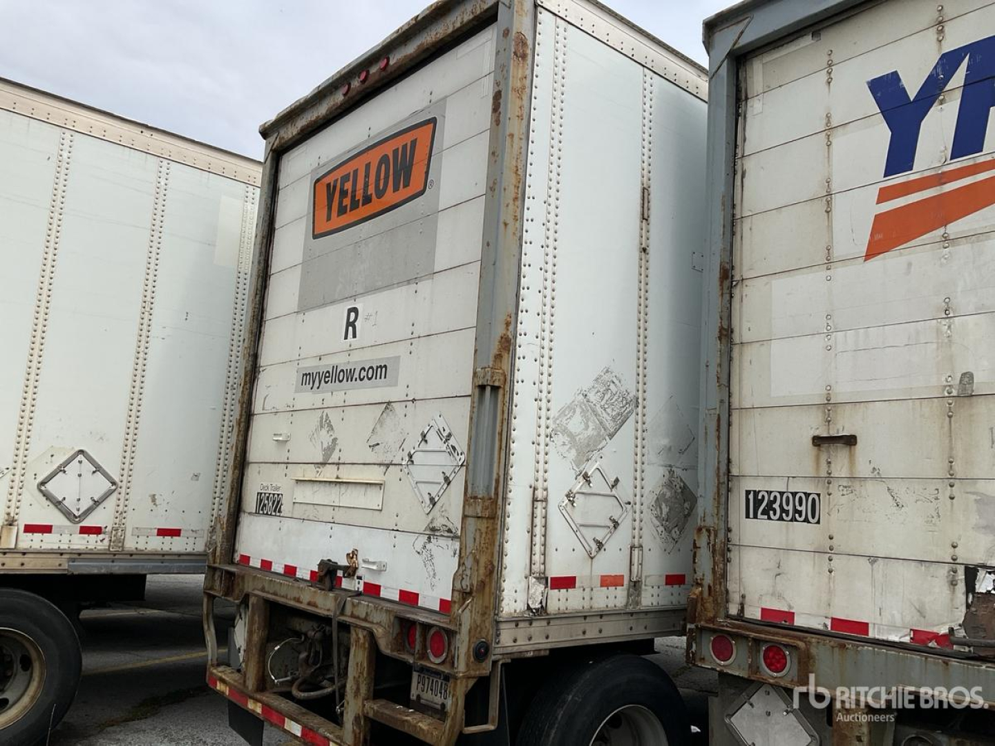 Trailer back view showing yellow 'YELLOW' sign, rear bumper, and rustic metal box on a Wabash trailer with wear marks.