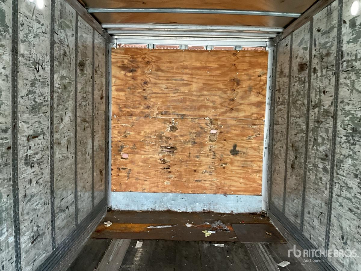 Rear interior of a cargo trailer with plywood bulkhead and metal sidewalls; empty floor with scattered debris.