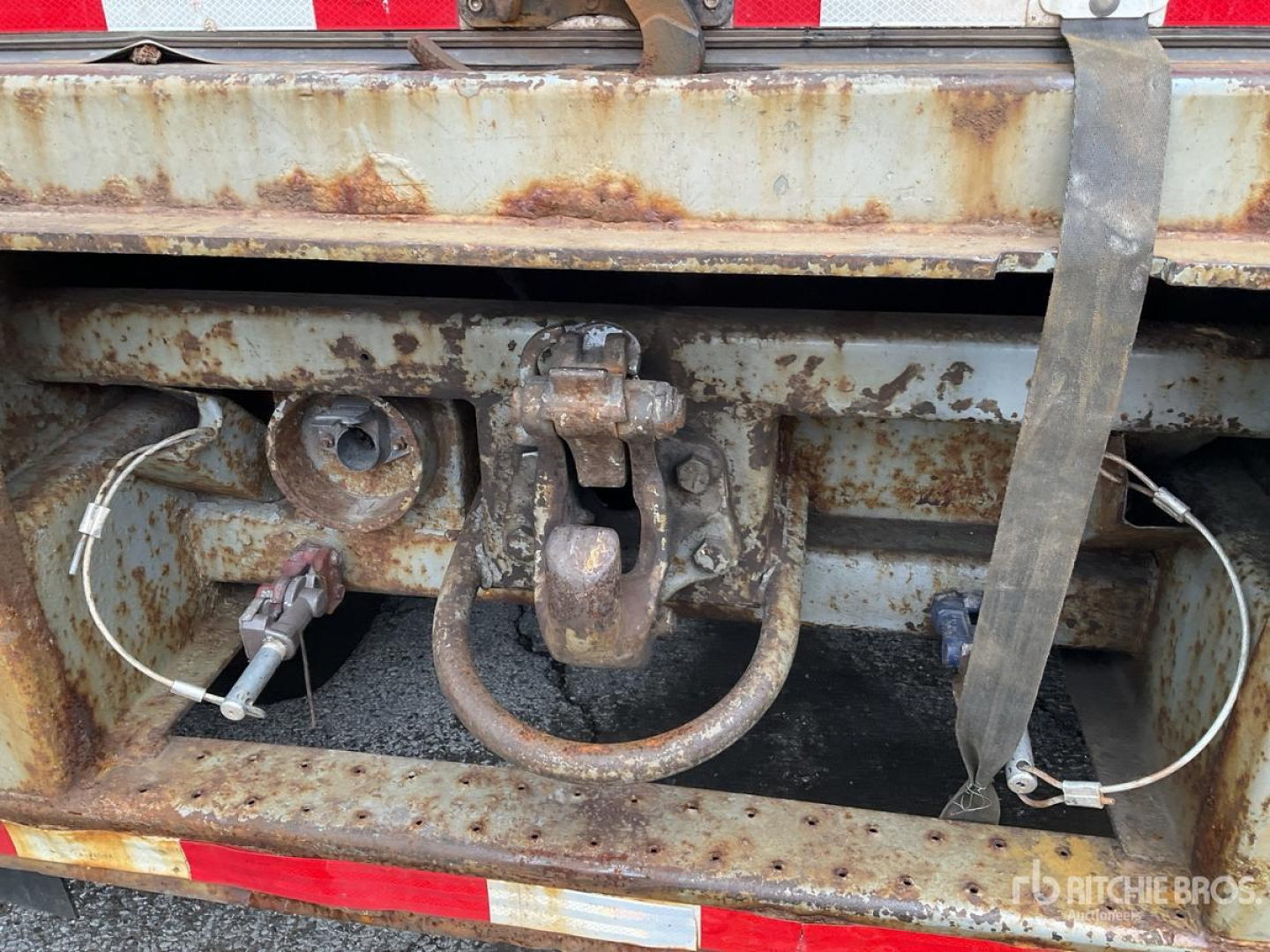 Trailer hitch and towing hardware on a rusted rear frame with coupler and safety chains visible