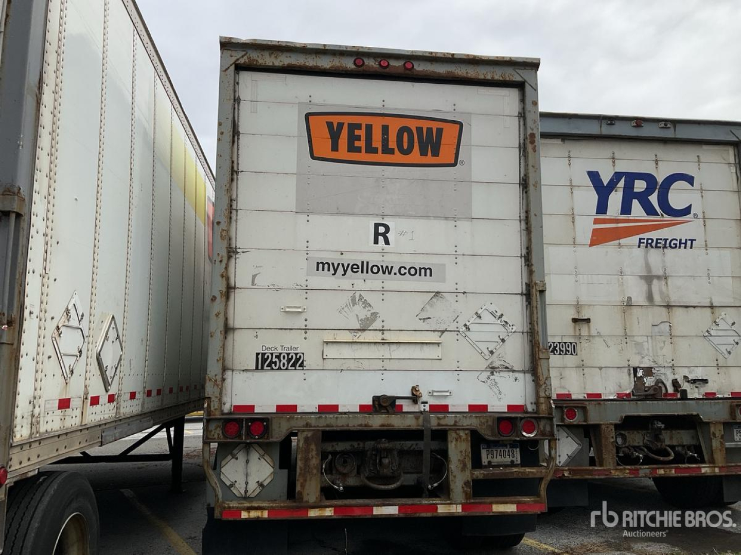 Trailer rear showing YELLOW sign and R code, with myyellow.com label, dirt marks, and trailer undercarriage details.