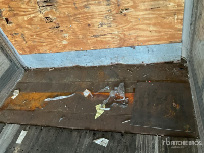 Trailer interior with wooden and metal floor, debris, and worn plywood wall. Visible text includes no legible labels; overall a rough cargo area.