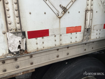 Trailer side with damaged rear lower panel and riveted metal, white paint, red reflective tape, and wheel visible.