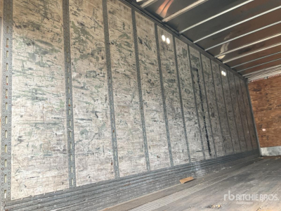 Trailer interior with silver metal walls and ribbed floor showing worn plywood header; no text readable.