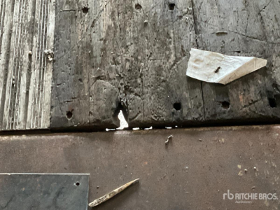 Trailer side with wooden planks and metal surface; small chipped edge with a white paper fragment. visible text not legible.
