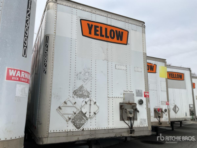 Trailer rear view with a bright orange YELLOW label on a white body, other trailers in the background; visible rear doors, latches, and warning diamond placards.
