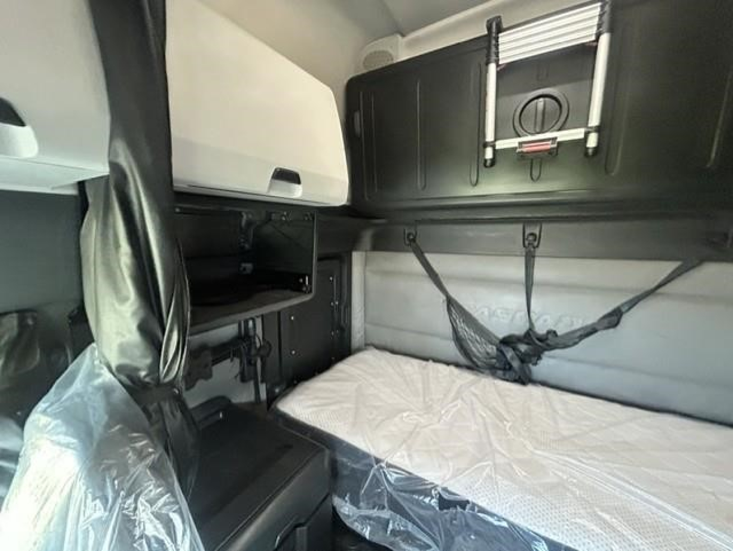 Freightliner Cascadia 126 sleeper cab interior showing bunk bed with white mattress, overhead storage cabinets, and straps.