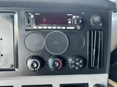 Dashboard with radio unit and climate controls in a Freightliner Cascadia 126 cabin showing a UHF radio, circular vents, and control knobs.