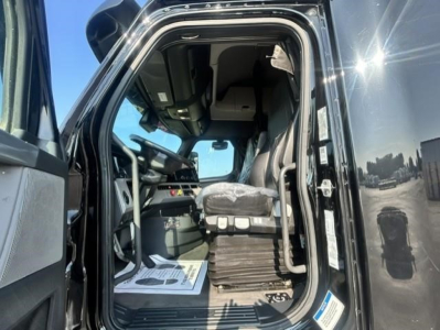 Cab interior of a 2022 Freightliner Cascadia 126 truck from the driver’s side open door showing the seat, dashboard, and entry area.