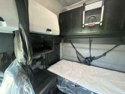 Freightliner Cascadia 126 sleeper cab interior showing bunk bed with white mattress, overhead storage cabinets, and straps.