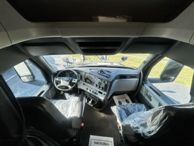 Freightliner Cascadia 126 truck cab interior view from front seat, steering wheel, dashboard, and seats visible; plastic seat covers and sun visor present.