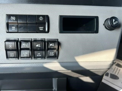Cab control panel of a Freightliner Cascadia showing switches and knobs with labels such as 'HSA OFF', 'LIGHT TEST', 'INT AXLE LOCK', 'PWR REL', 'AIR SLIDE', and 'SUSP DUMP'.