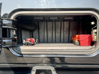 Storage compartment in a Freightliner Cascadia showing a red toolbox and a coiled hose inside the under-cab storage area.