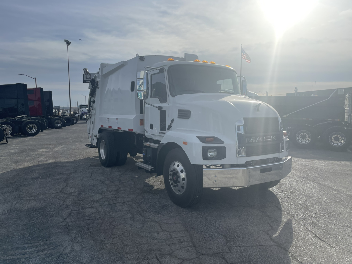 Mack MD7 garbage truck in a lot, front-right view showing cab and refuse body with chrome bumper and daytime running lights.