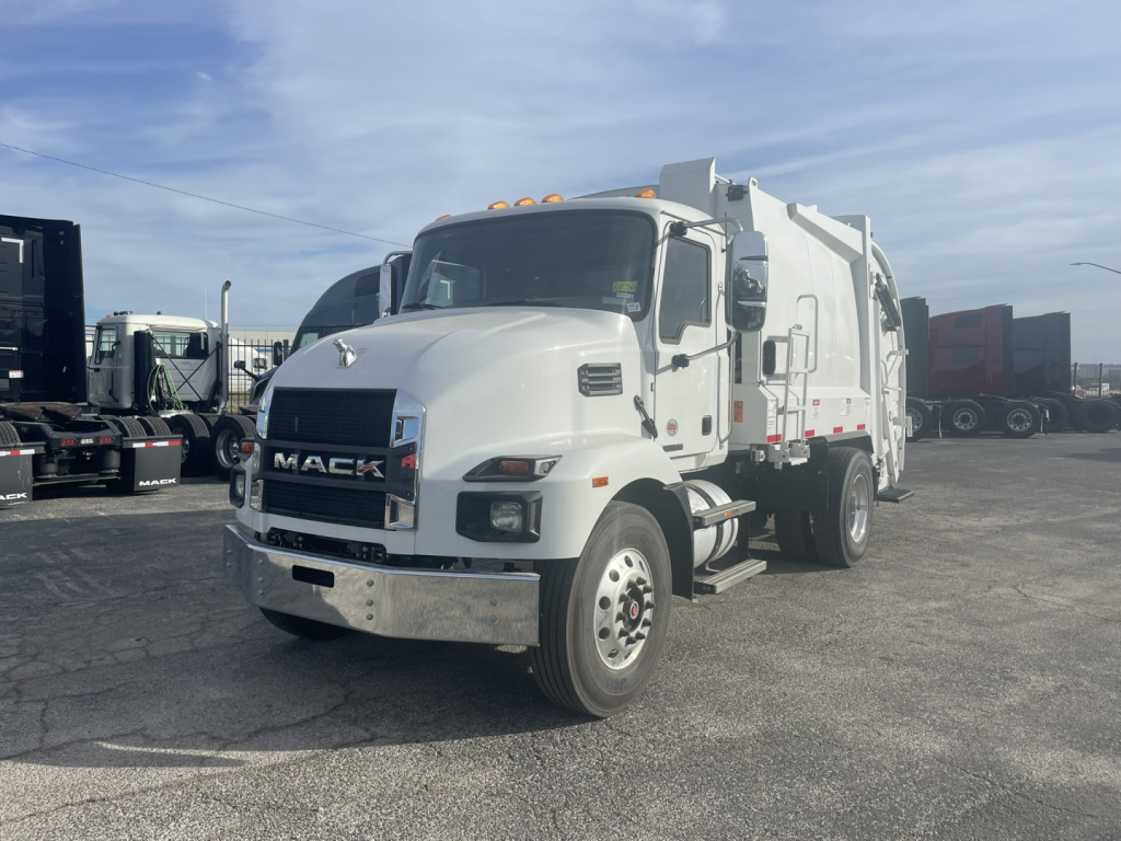 Truck from front-left view with Mack MD7 cab and refuse body. Visible text includes 'MACK' on grille. Side mirrors, headlights, and front bumper are chrome. 