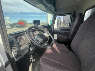 Front cabin of a new 2026 Mack MD7 refuse truck showing steering wheel, dashboard, and driver seat with fabric upholstery.