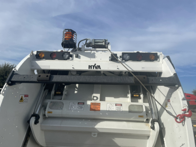 Rear view of a Mack MD7 refuse truck body showing hydraulic components, warning labels, and tailgate with hazard lights and branding HYVA.